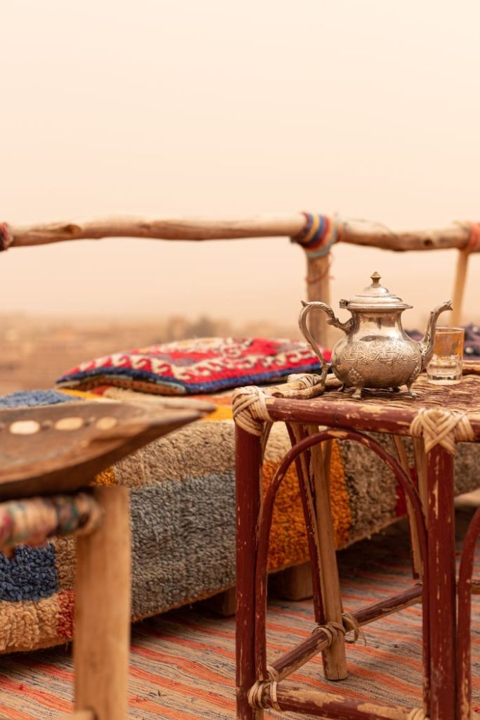 Warm and inviting outdoor tea setup with a rustic vibe, featuring a silver teapot and colorful textiles.