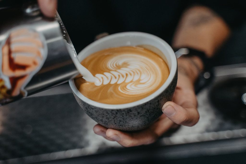 Close-up of a barista pouring milk to create intricate latte art in a ceramic cup.