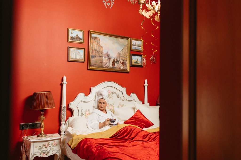 Woman enjoying tea in a vintage bedroom with vibrant red walls and elegant decor.